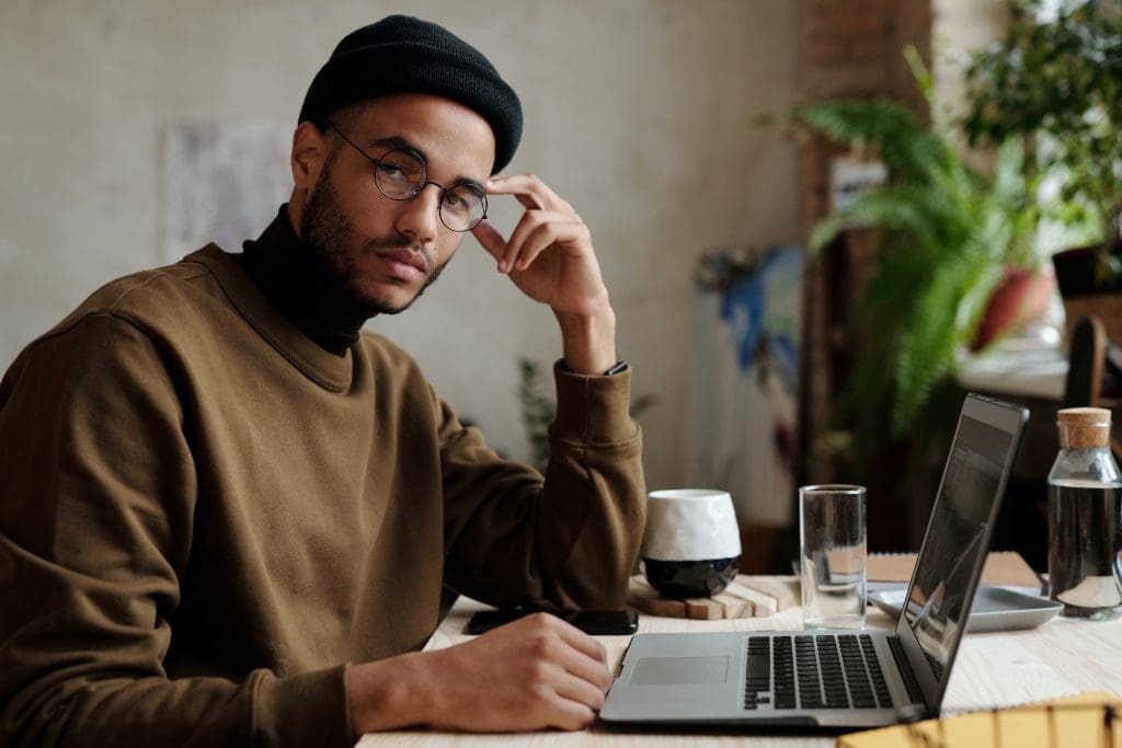 A web designer in a brown sweater and black beanie sits in front of laptop